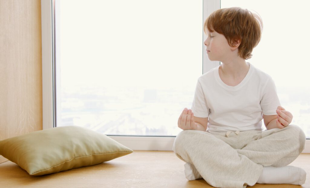 Rothaariger Junge sitzt im Schneidersitz auf dem Boden und praktiziert Kinder-Yoga