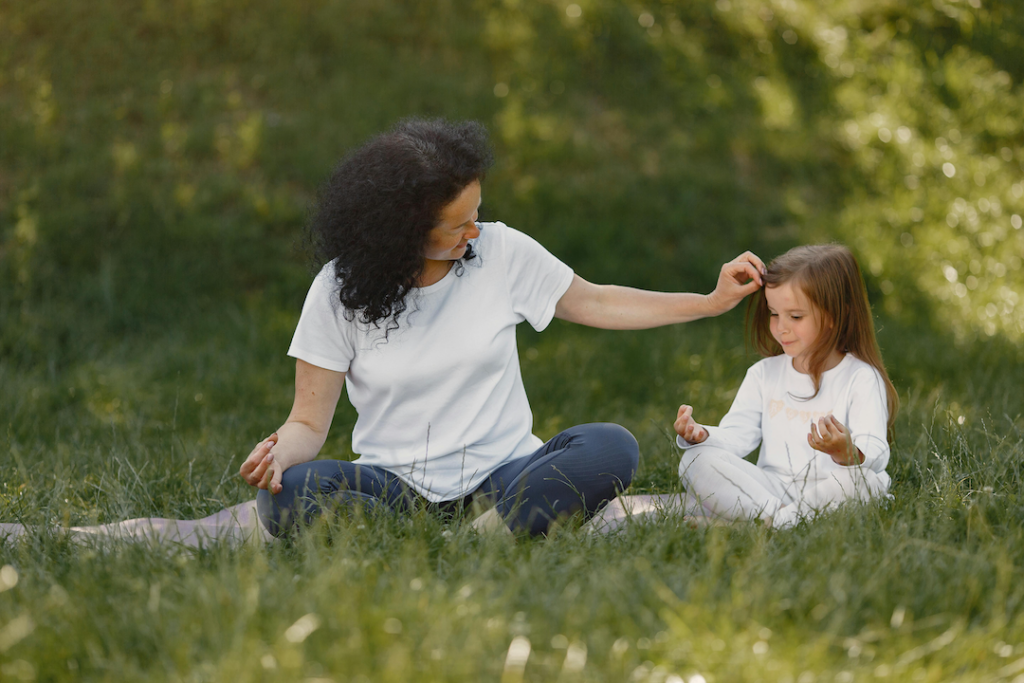 Mutter und Tochter sitzen auf einer Yogamatte auf der Wiese und praktizieren Eltern-Kind-Yoga